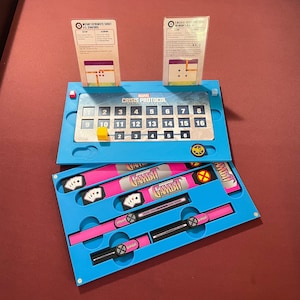 May include: A Marvel Crisis Protocol board game set with blue and pink components. The set includes a game board with numbered spaces, cards, and components labeled "Gambit". Two informational cards are also included.