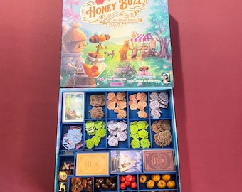 May include: A blue and white game box with the title "Honey Buzz" and a bee illustration. The box is open and contains various game pieces, including wooden tokens, cards, and plastic figures.
