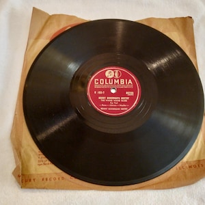 May include: A vintage black vinyl record from Columbia Records, featuring a red label with white text. The record is in a tan paper sleeve. The label reads "Benny Goodman Sextet" and "The Wang Wang Blues."