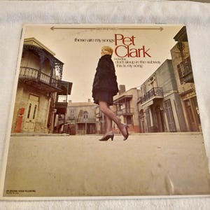 Peut inclure: Pochette de l'album vinyle vintage de Pet Clark, "These Are My Songs". La couverture présente une femme en manteau noir marchant dans une rue avec des bâtiments en arrière-plan. Le titre de l'album et le nom de l'artiste sont affichés.