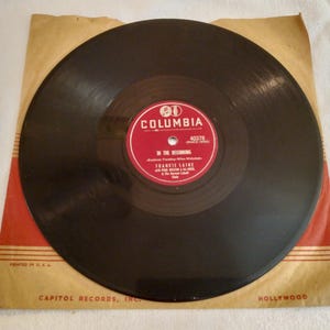 May include: A vintage vinyl record by Frankie Laine, titled "In The Beginning," is displayed in its original sleeve. The record label is red with white text and the Columbia Records logo. The sleeve is tan with red accents and the Capitol Records logo.