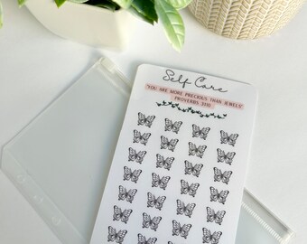 Op de afbeelding: Een witte kaart met zwarte vlinder stickers en de tekst "Self Care" en "You are more precious than jewels" met de bijbelverwijzing "Proverbs 3:10". De kaart heeft ook de tekst "X 28 Icons = Goals = GRACEFULLY SEEKING".