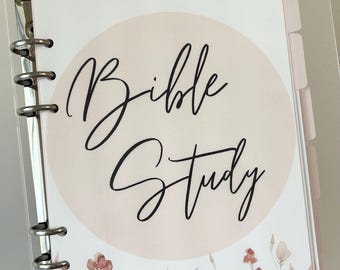 May include: A Bible Study binder with a soft pink circular design and the words "Bible Study" in elegant black script. The binder features floral watercolor artwork at the bottom and the text "Gracefully Seeking" at the top. The binder is held open by silver metal rings.