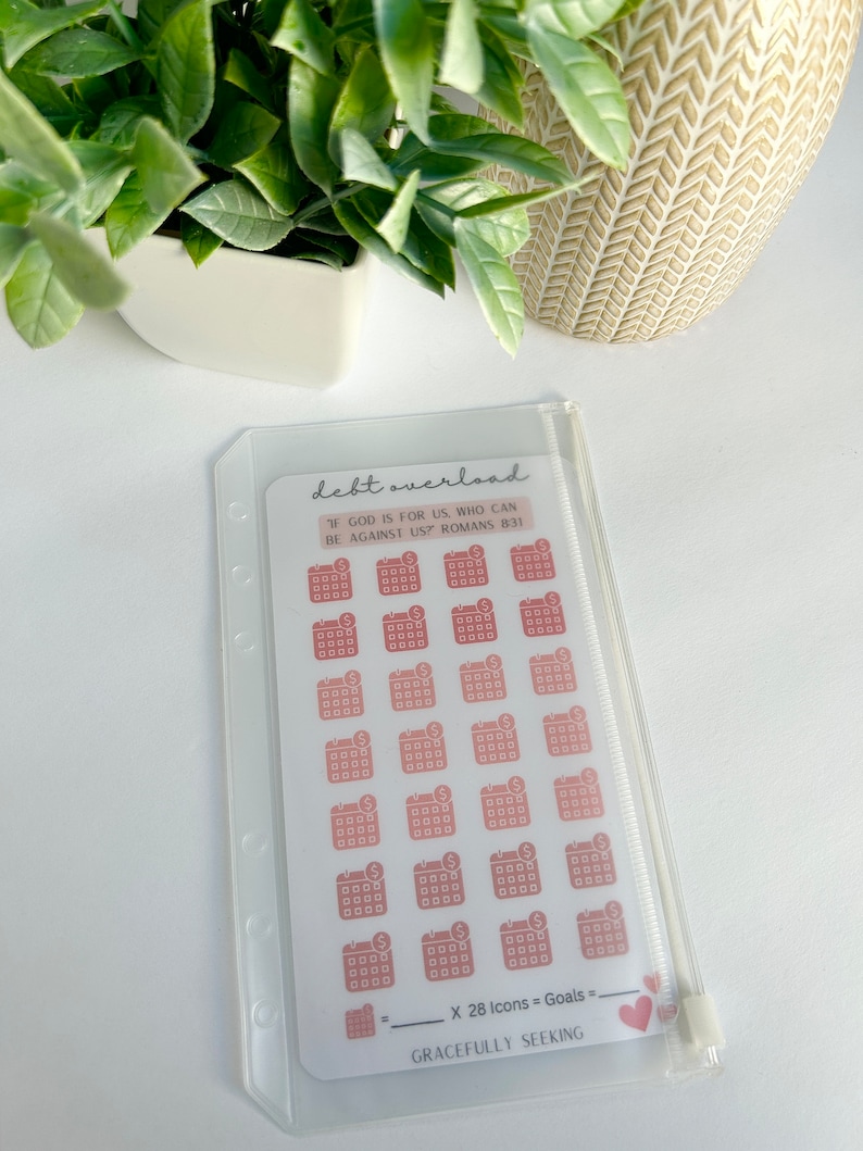 May include: A clear plastic pouch with a white card inside. The card has a pink and white design with the text "debt overload" and "If God is for us, who can be against us? Romans 8:31". There are 28 pink and white calendar icons with a dollar sign on each icon. The text "X 28 Icons = Goals =" is written on the card. The card also has the text "GRACEFULLY SEEKING".