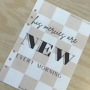 以下が含まれることがあります： 白とベージュの市松模様のプランナーページに、黒い文字で「his mercies are NEW EVERY MORNING」と書かれています。右上に「GRACEFULLY SEEKING」という文字が書かれています。左下に「lamentation 3:22-23」という文字が書かれています。