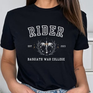 May include: Black t-shirt with white text that reads "Rider Est 2023 Basgiath War College". The text is surrounded by a graphic of a winged creature with a sword and a wreath.