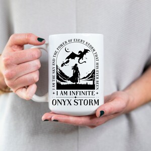 Puede incluir: Taza de cer&aacute;mica blanca con un dise&ntilde;o negro que representa a una mujer de pie frente a una cordillera con un drag&oacute;n volando por encima. El texto dice "I am the sky and the power of every storm that has ever been + I am infinite + Onyx Storm".