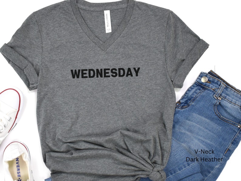 May include: Dark heather grey V-neck t-shirt with the word "WEDNESDAY" printed in black on the front.