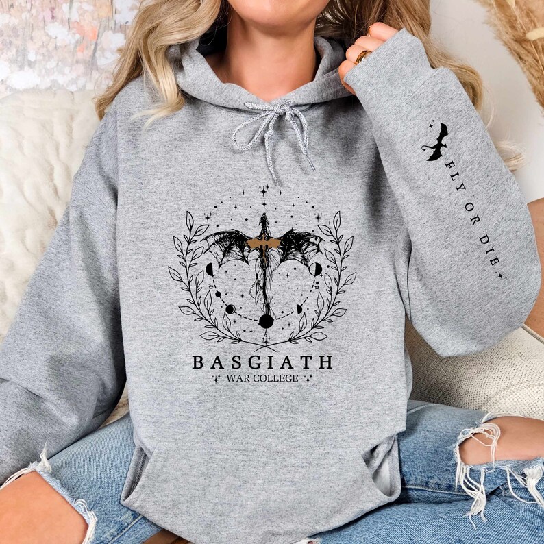 Hoodie featuring the Basgiath War College emblem, ideal for fans of dragons and fantasy books. Front design showcases the college's prestige, while the sleeve displays a dragon beside the quote Fly or Die. Perfect for Fourth Wing enthusiasts.