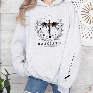 Hoodie featuring the Basgiath War College emblem, ideal for fans of dragons and fantasy books. Front design showcases the college's prestige, while the sleeve displays a dragon beside the quote Fly or Die. Perfect for Fourth Wing enthusiasts.