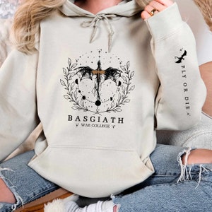 Hoodie featuring the Basgiath War College emblem, ideal for fans of dragons and fantasy books. Front design showcases the college's prestige, while the sleeve displays a dragon beside the quote Fly or Die. Perfect for Fourth Wing enthusiasts.