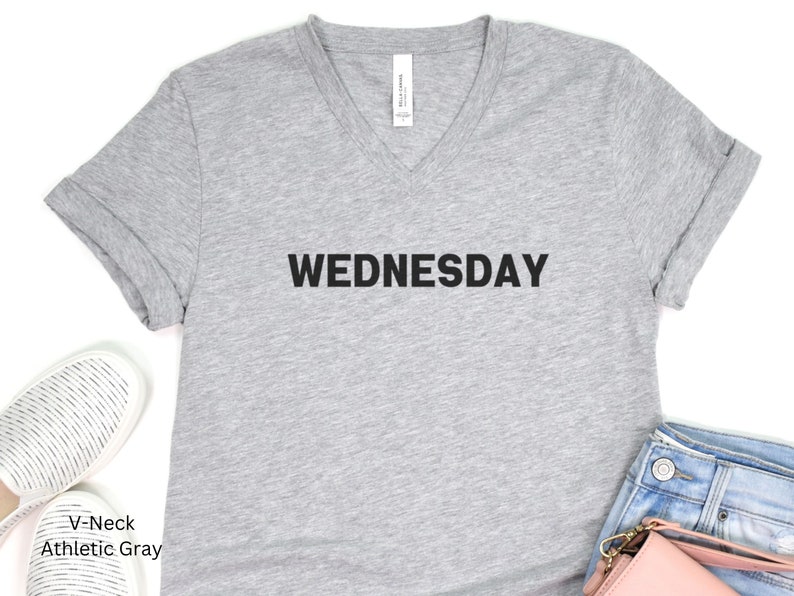 May include: A gray V-neck t-shirt with the word "WEDNESDAY" printed in black on the front.