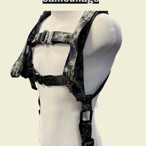 May include: A black and green camouflage squat harness with adjustable straps and buckles. The harness is designed for weightlifting and features a D-ring on the back.