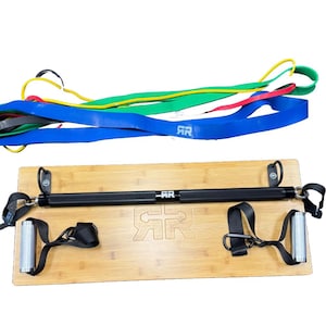 May include: A black exercise bar with two handles attached to a wooden board. The bar has a metal loop on each end. There are five resistance bands in different colors, including red, yellow, green, and blue, stacked on top of the board.
