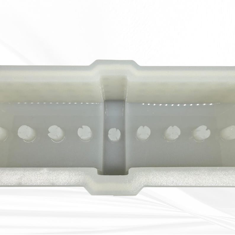 Op de afbeelding: Een close-up van een doorschijnende, gebroken witte plastic container. De container heeft een rechthoekige vorm met een reeks cirkelvormige uitsparingen langs de onderrand. Het ontwerp omvat een verhoogd middengedeelte en een getextureerde basis.