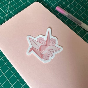 May include: Pink origami crane sticker with pink cherry blossoms and the text "@riceclub.co" on a pink notebook.
