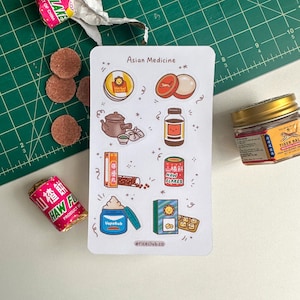 May include: A sheet of stickers featuring illustrations of Asian medicine products, including Tiger Balm, VapoRub, Haw Flakes, and herbal tea. The stickers are on a white background with a green and white grid pattern in the background.