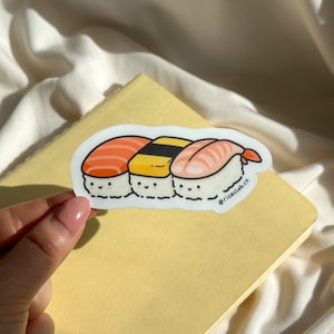 May include: A sticker of three cartoon sushi rolls with smiling faces. The sushi rolls are salmon, yellowtail, and tuna. The sticker has the text "@riceclub.co" on the bottom right corner.