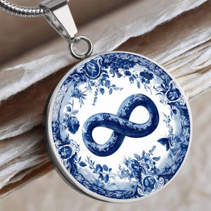 May include: A silver-toned pendant necklace featuring a round, blue and white design. The pendant showcases a blue infinity symbol surrounded by floral patterns and a butterfly on a white background. The necklace has a silver chain.