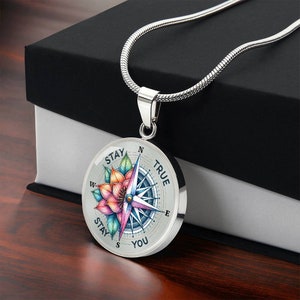 May include: Silver necklace with a compass pendant featuring a colorful flower design and the words "Stay True Stay You".