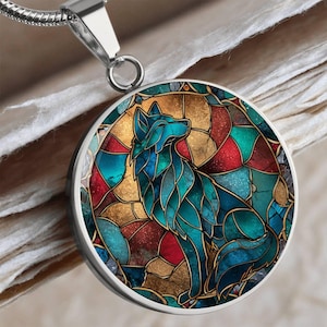 May include: A silver-toned pendant necklace featuring a colorful wolf design. The pendant has a round shape with a stained-glass style wolf in shades of teal, blue, red, and gold. The chain is a thin, silver-colored snake chain.