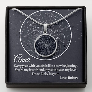 May include: A silver pendant necklace with a dark blue circular pendant featuring a white star map design. The necklace is presented in a black gift box with the name "Anna" and a romantic message printed on the inside.