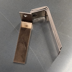 May include: Four silver metal brackets with a 90-degree angle. The brackets are stacked on top of each other.