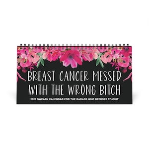 May include: A desk calendar with a black background and the text "BREAST CANCER MESSED WITH THE WRONG BITCH". The calendar has a floral design with pink flowers and green leaves. The text "2026 SWEARY CALENDAR FOR THE BADASS WHO REFUSES TO QUIT" is also included.