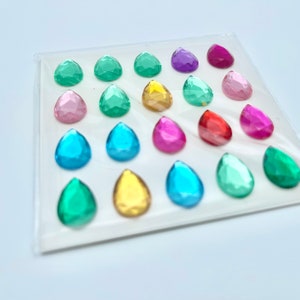Op de afbeelding: Een vel met kleurrijke, traanvormige edelstenen, perfect voor knutselen of decoreren. De edelstenen zijn in rijen gerangschikt en verkrijgbaar in verschillende kleuren, waaronder roze, blauw, groen, geel, rood en paars.