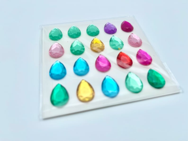 Op de afbeelding: Een vel met kleurrijke, traanvormige edelstenen, perfect voor knutselen of decoreren. De edelstenen zijn in rijen gerangschikt en verkrijgbaar in verschillende kleuren, waaronder roze, blauw, groen, geel, rood en paars.