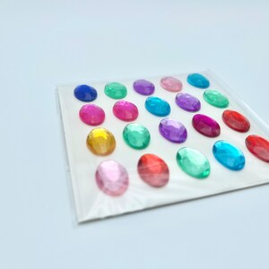Op de afbeelding: Een vel met kleurrijke ovale edelstenen, perfect voor knutselen of decoreren. De edelstenen zijn in rijen gerangschikt en zijn verkrijgbaar in verschillende kleuren, waaronder blauw, groen, rood, roze en geel.