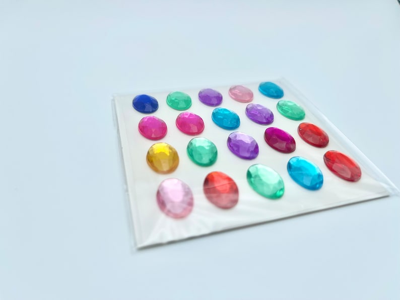 Op de afbeelding: Een vel met kleurrijke ovale edelstenen, perfect voor knutselen of decoreren. De edelstenen zijn in rijen gerangschikt en zijn verkrijgbaar in verschillende kleuren, waaronder blauw, groen, rood, roze en geel.