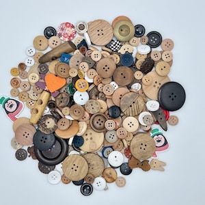 Op de afbeelding: Een grote verzameling van verschillende knopen in verschillende kleuren, vormen en maten. De knopen zijn gemaakt van hout, plastic en metaal. Sommige knopen hebben een decoratief ontwerp, terwijl andere simpel zijn.