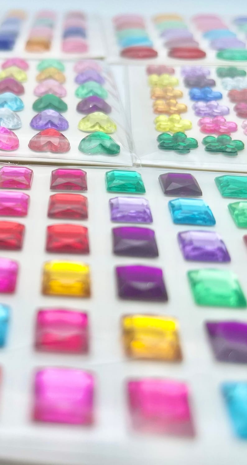 Op de afbeelding: Assortiment van kleurrijke, heldere en iriserende vierkante edelstenen. De edelstenen zijn gerangschikt in rijen op een witte achtergrond.