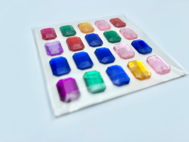 Op de afbeelding: Een vel met kleurrijke, zelfklevende, edelsteenvormige stickers. De stickers zijn gerangschikt in een rasterpatroon en zijn verkrijgbaar in verschillende kleuren, waaronder rood, blauw, groen, geel, roze en paars.