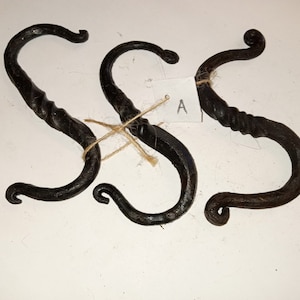 May include: Three black, hand-forged metal S-hooks. Each hook has a twisted central section and curved ends. The hooks are tied together with twine and a small tag labeled "A".