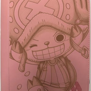 May include: A light pink binder featuring a monochromatic brown line art illustration of the character Tony Tony Chopper from One Piece. The character wears a large hat with an X symbol, has a wide grin, and is surrounded by small cherry blossom petals.