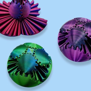 May include: Three decorative spheres with interlocking gears. The spheres are made of a shiny plastic material and are coloured purple, green, and a mix of blue and green.