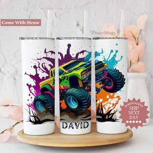 May include: Three white stainless steel tumblers with a monster truck graphic. The tumblers have a colorful paint splatter design and the name "DAVID" is printed on one of the tumblers.
