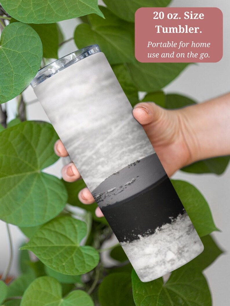 May include: A 20 ounce stainless steel tumbler with a black and white abstract design. The tumbler is held in a hand and is surrounded by green leaves. "20 oz. Size Tumbler. Portable for home use and on the go." is written in pink text on a white background.