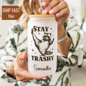 May include: White 16oz reusable glass tumbler with a bamboo lid and a black and white illustration of a raccoon doing yoga with the text "Stay Trashy Samantha".
