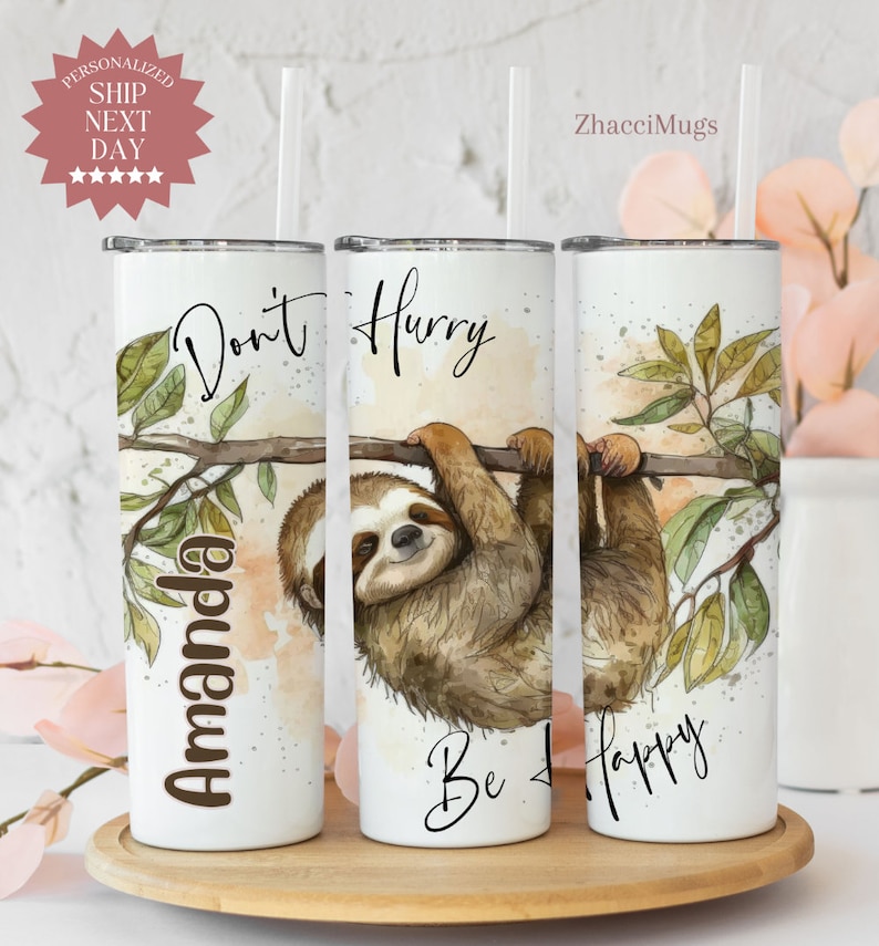 May include: Three white stainless steel tumblers with a watercolor sloth design. The tumblers have the text "Don't Hurry Be Happy" and "Amanda" on them.