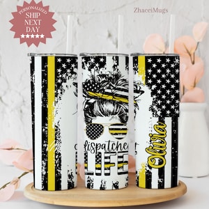 May include: Three stainless steel tumblers with a white background and a thin yellow stripe. The tumblers feature a black and white illustration of a woman with a bun, sunglasses, and a thin yellow ribbon. The text "dispatchers life" is printed on the middle tumbler. The text "Olivia" is printed on the right tumbler.