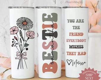 May include: Three white insulated tumblers with floral and text designs. One features a daisy and pink flowers, another says "BESTIE", and the third reads "YOU ARE THE FRIEND EVERYBODY WISHES THEY HAD" with a name. Each comes with a straw.