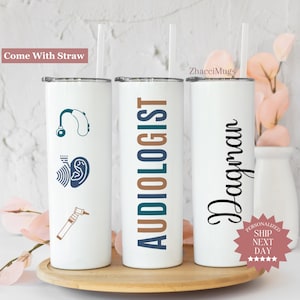 May include: White insulated tumbler with a straw. One tumbler has the word "AUDIOLOGIST" in teal and brown. Another has the name "Dagmar" in black script. The third tumbler has hearing-related graphics.