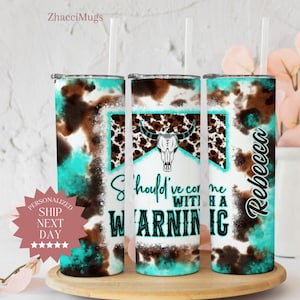 May include: A turquoise and brown tumbler with a cow skull design and the text "Should've come with a warning". The tumbler is personalized with the name "Rebecca".
