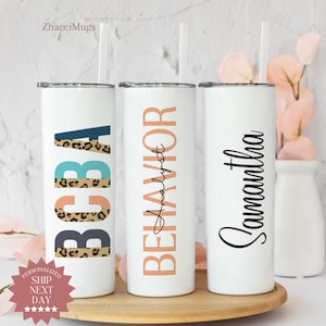 May include: Three white stainless steel tumblers with different designs. The first tumbler has the word "BOBA" in colorful letters with a leopard print design. The second tumbler has the word "BEHAVIOR Analyst" in peach colored letters. The third tumbler has the name "Samantha" in black cursive writing.
