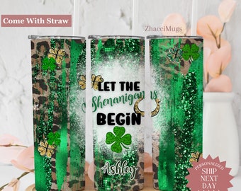 May include: A green and gold glitter tumbler with the text "Let the Shenanigans Begin" and a four-leaf clover. The tumbler is personalized with the name "Ashley".