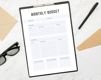 May include: A black clipboard with a "MONTHLY BUDGET" template, a black pen, eyeglasses, and envelopes. The template includes sections for income and expenses, with fields for date, description, and amount. The layout is clean and organized.