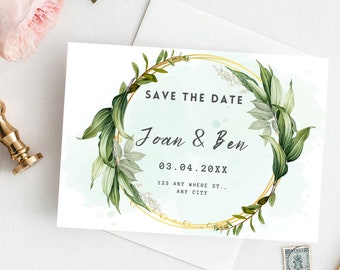 May include: A white Save the Date card featuring a gold circular frame adorned with green leaves. The text reads "SAVE THE DATE", followed by names and a date. An address is also included on the card.